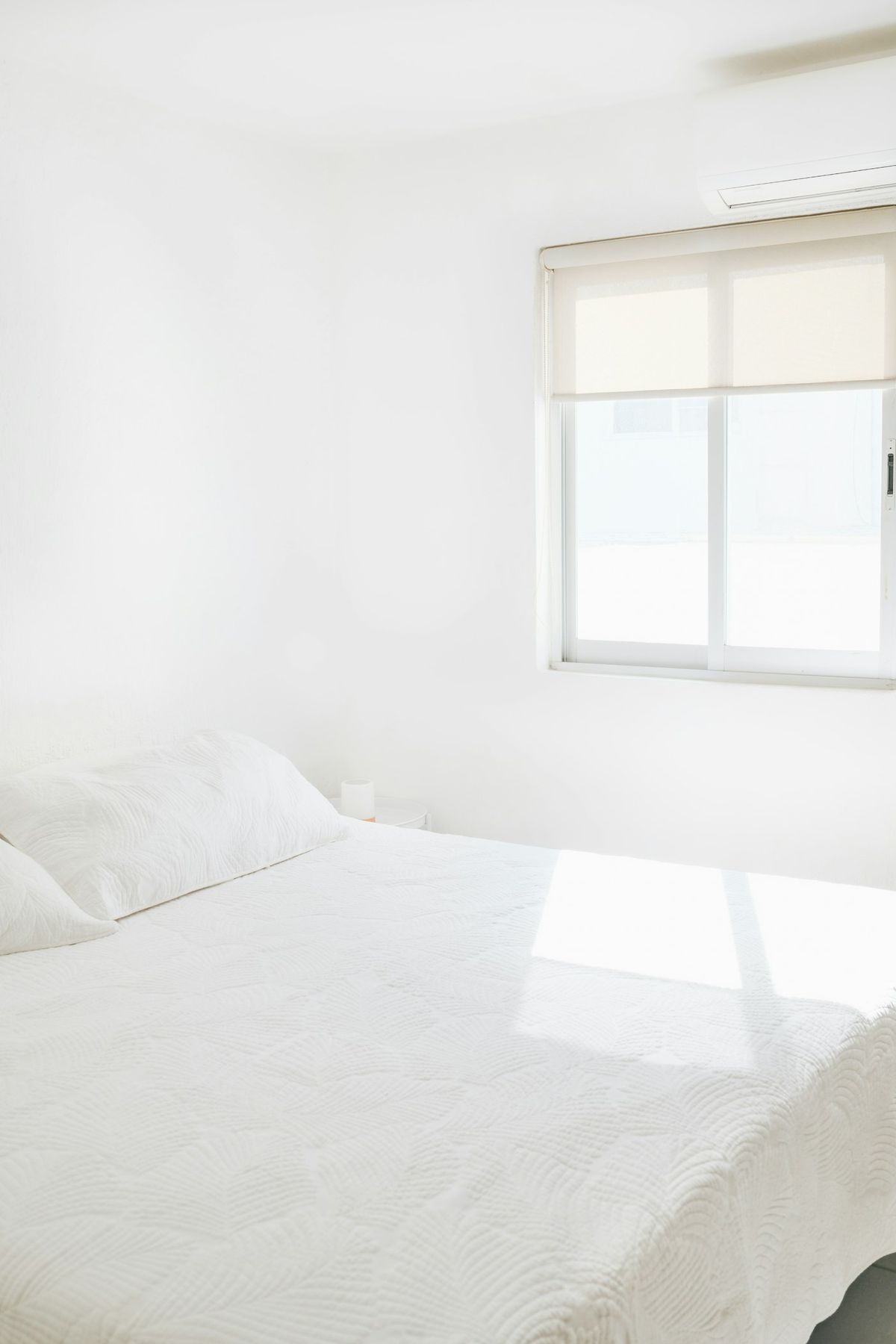A bright white bedroom with a freshly made bed and sunlight across the linen